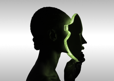 Silhouette of person holding translucent green face-shaped mask against grey background