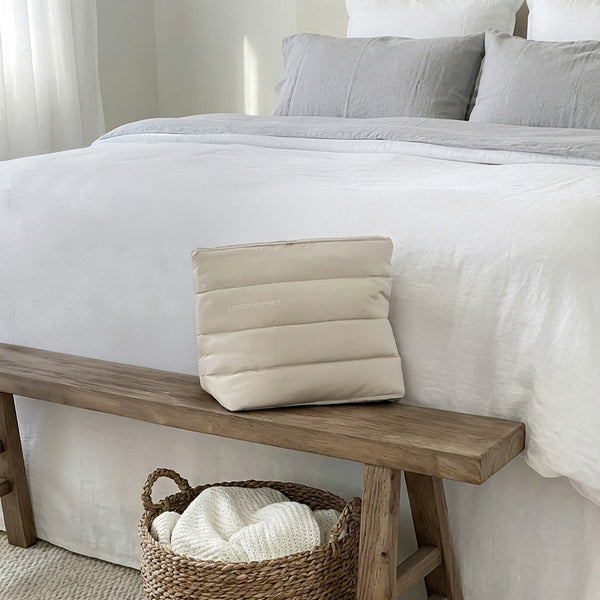 Large cream luxury device bag with quilted design on wooden bench in neutral bedroom