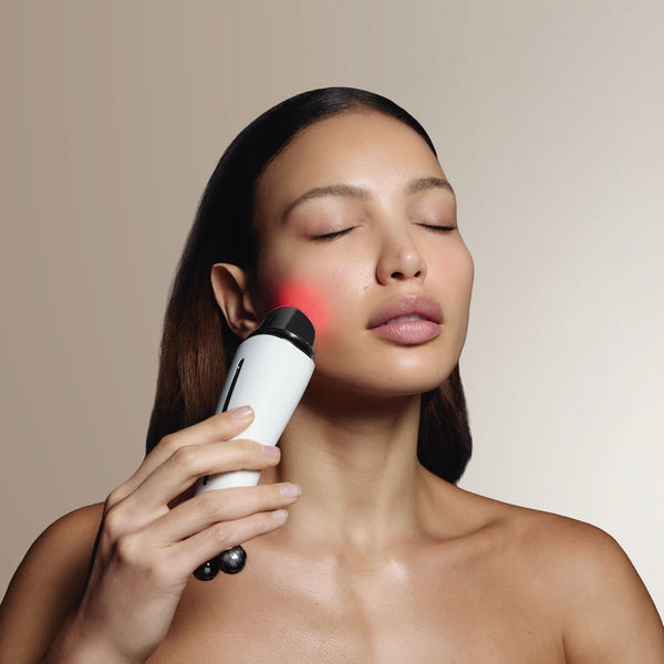 Woman using white handheld Sculpta by Déesse PRO facial device with red light on cheek
