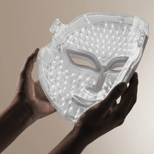 Transparent LED light therapy mask held by hands, designed for facial skincare treatment