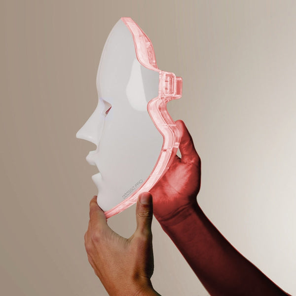 Hands holding a white and pink translucent facial mask with a strap