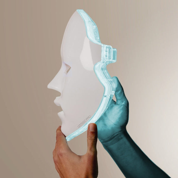 Hand holding translucent white and blue facial mask with sculpted features against neutral background