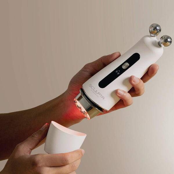 White handheld Sculpta by Déesse PRO facial device with dual metal spheres and red light therapy feature