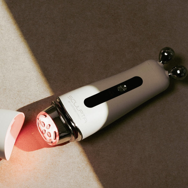 White and black handheld Sculpta by Déesse PRO facial device with dual metal rollers and red light therapy feature