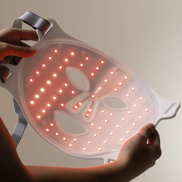 White LED light therapy face mask with adjustable grey straps held by hands